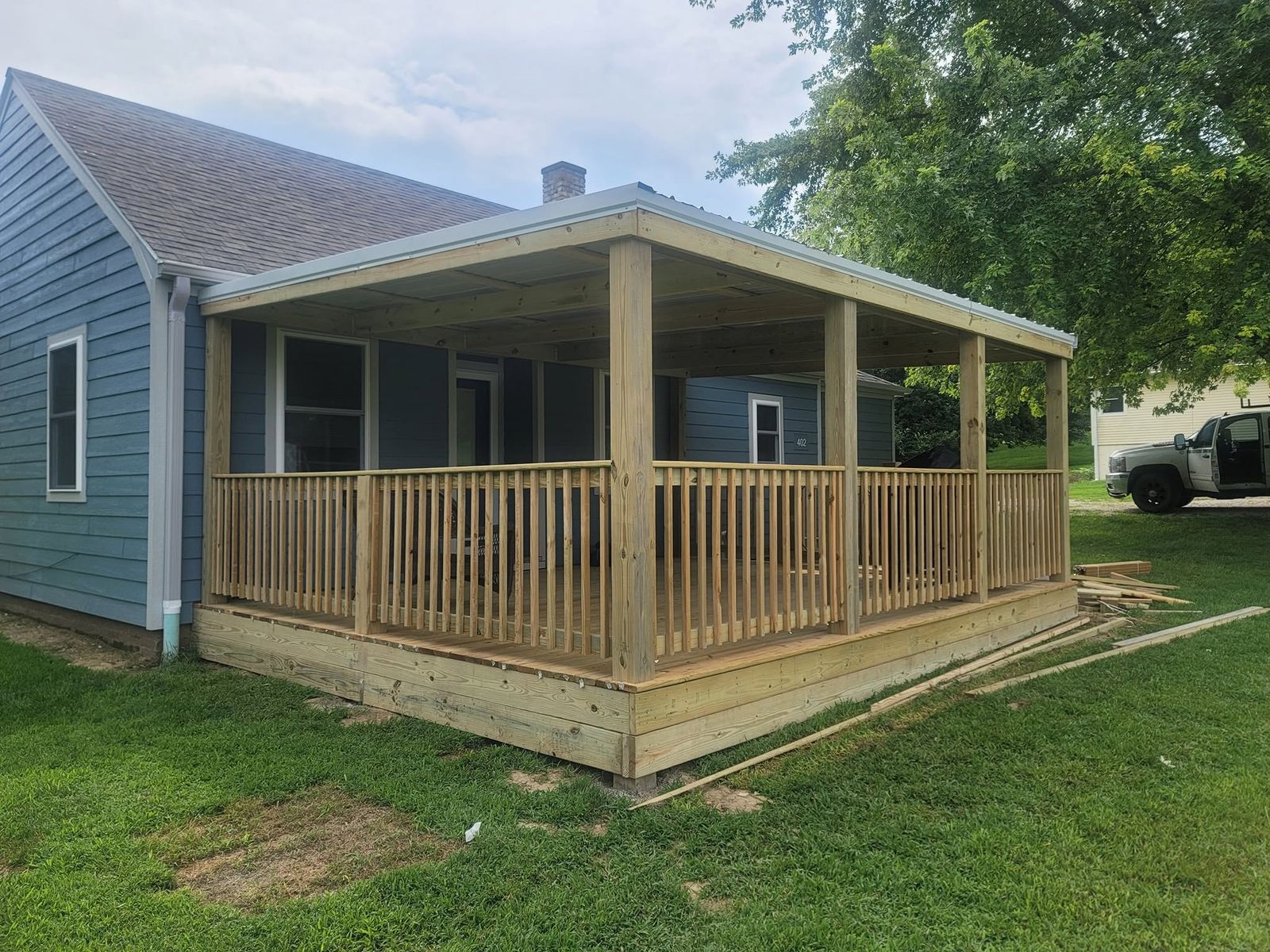 New covered wood porch with a metal roof and a square wood railing on a blue house