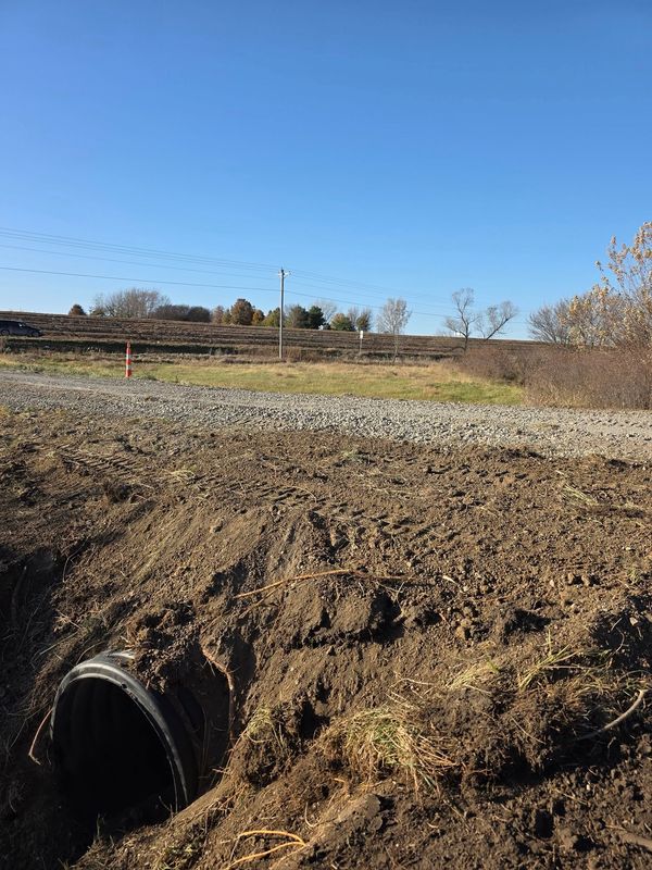 End of a culvert pipe set in the ground beside a gravel road