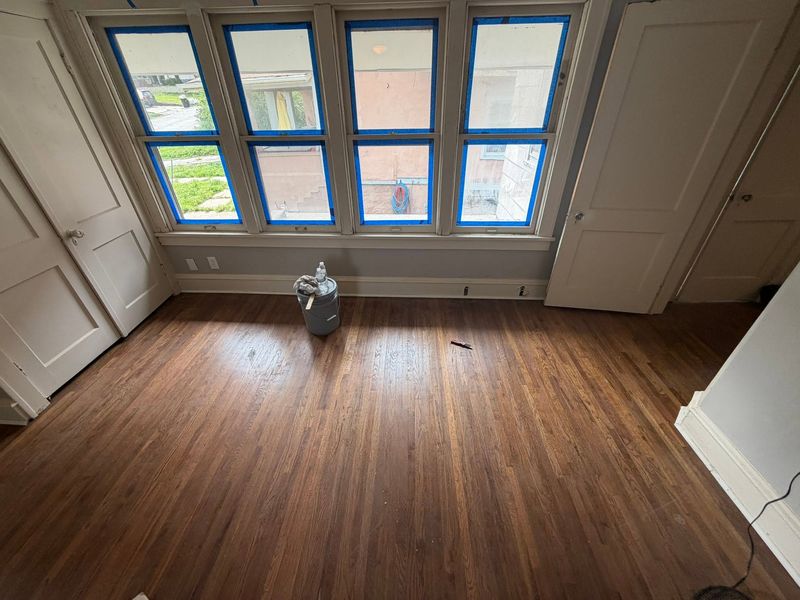 Wood floor mid-refinish in a bright room with a row of windows