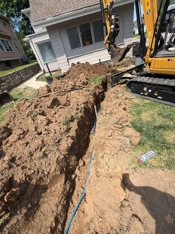 Compact excavator digging a trench across a front yard