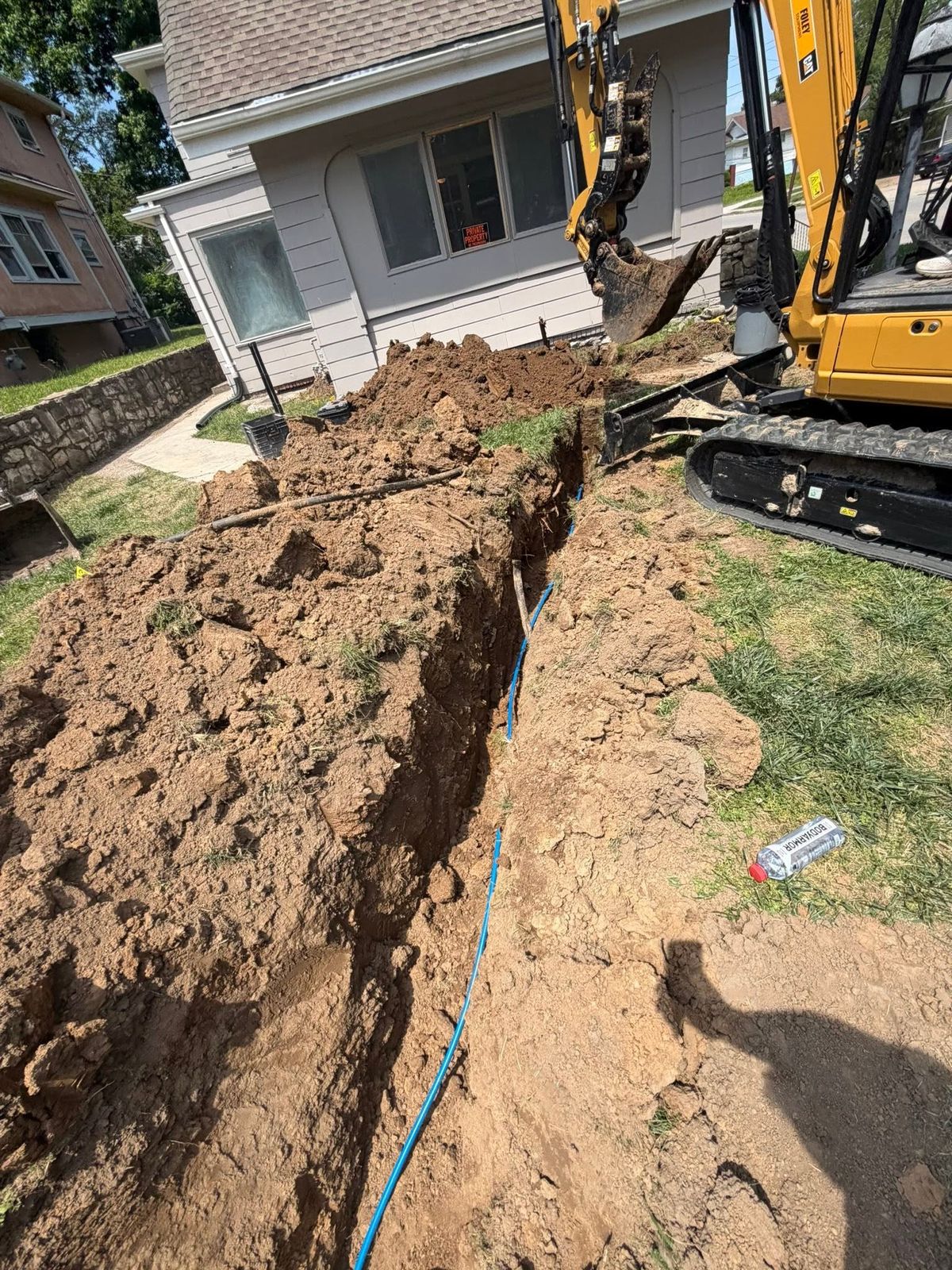 Compact excavator digging a trench across a front yard for buried conduit