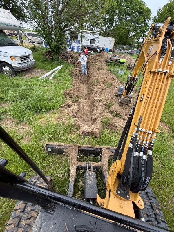 View from the excavator cab trenching across a grassy rural lot